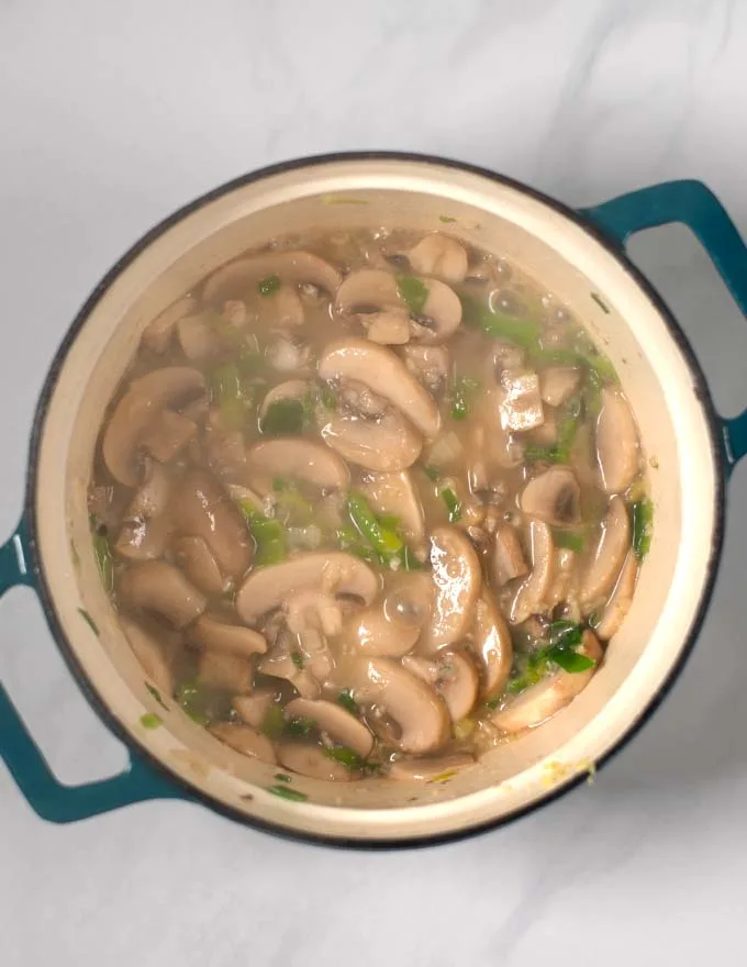 Mushrooms and scallions are fried in a large pot.