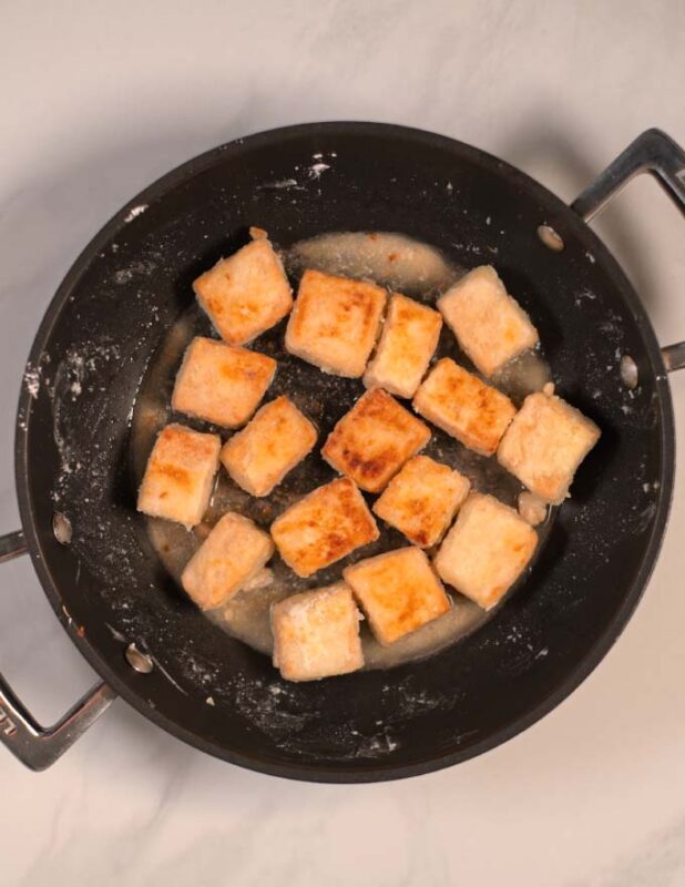 Tofu cubes are fried cripsy and golden brown in a pan.