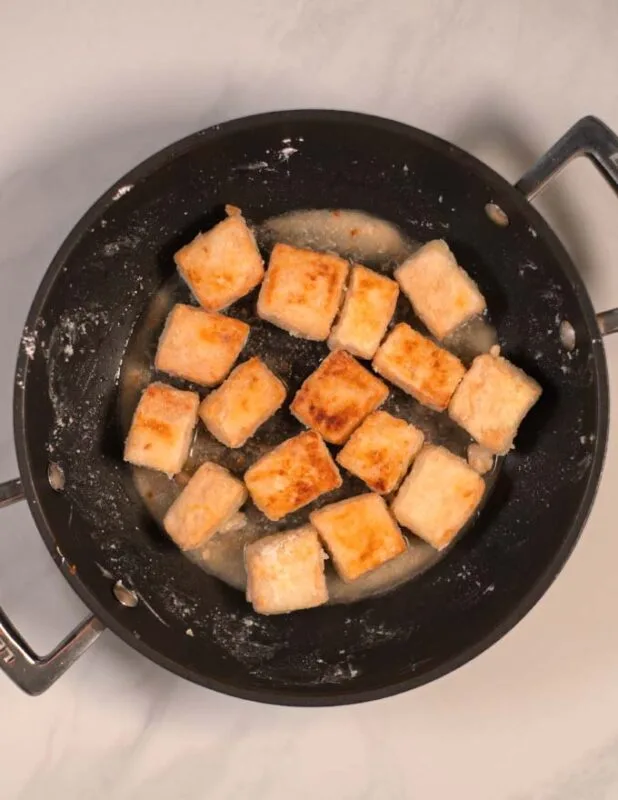 Tofu cubes are fried cripsy and golden brown in a pan.