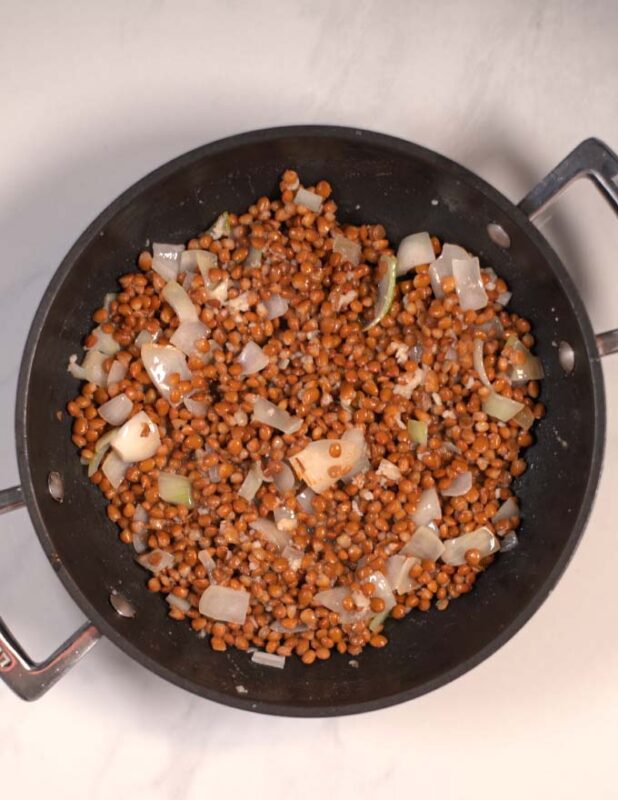 Onions and lentils are cooked in a pan.