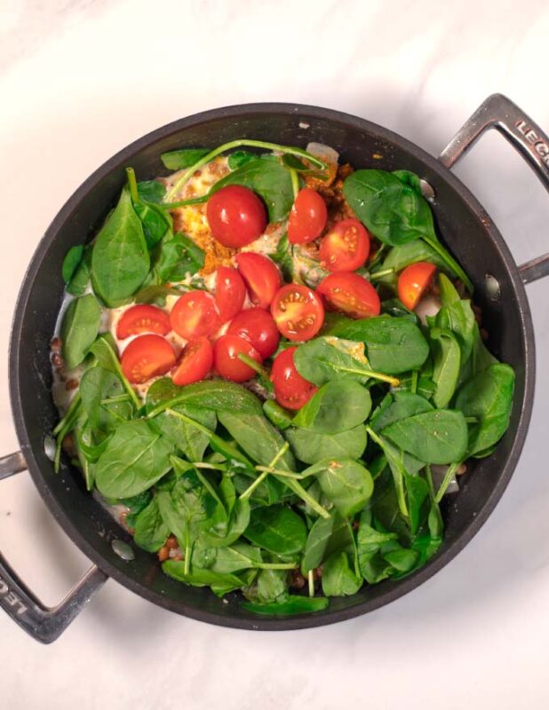 Halved cherry tomatoes are mixed into the pan.