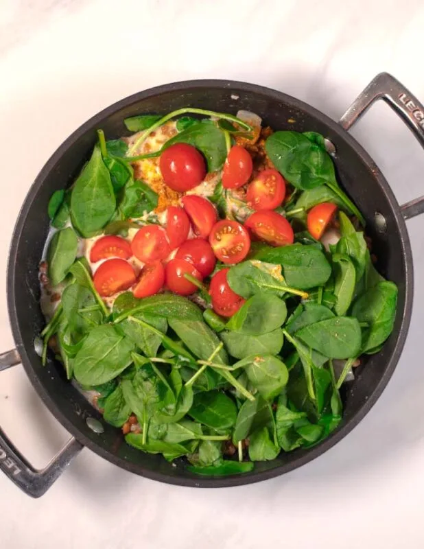 Halved cherry tomatoes are mixed into the pan.