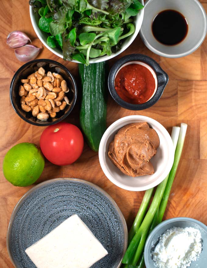 Ingredients needed to make Tofu Salad are assembled on a wooden cutting board.