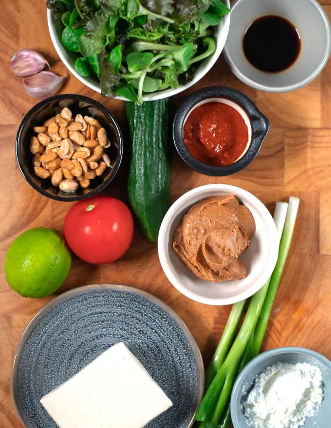 Ingredients needed to make Tofu Salad are assembled on a wooden cutting board.