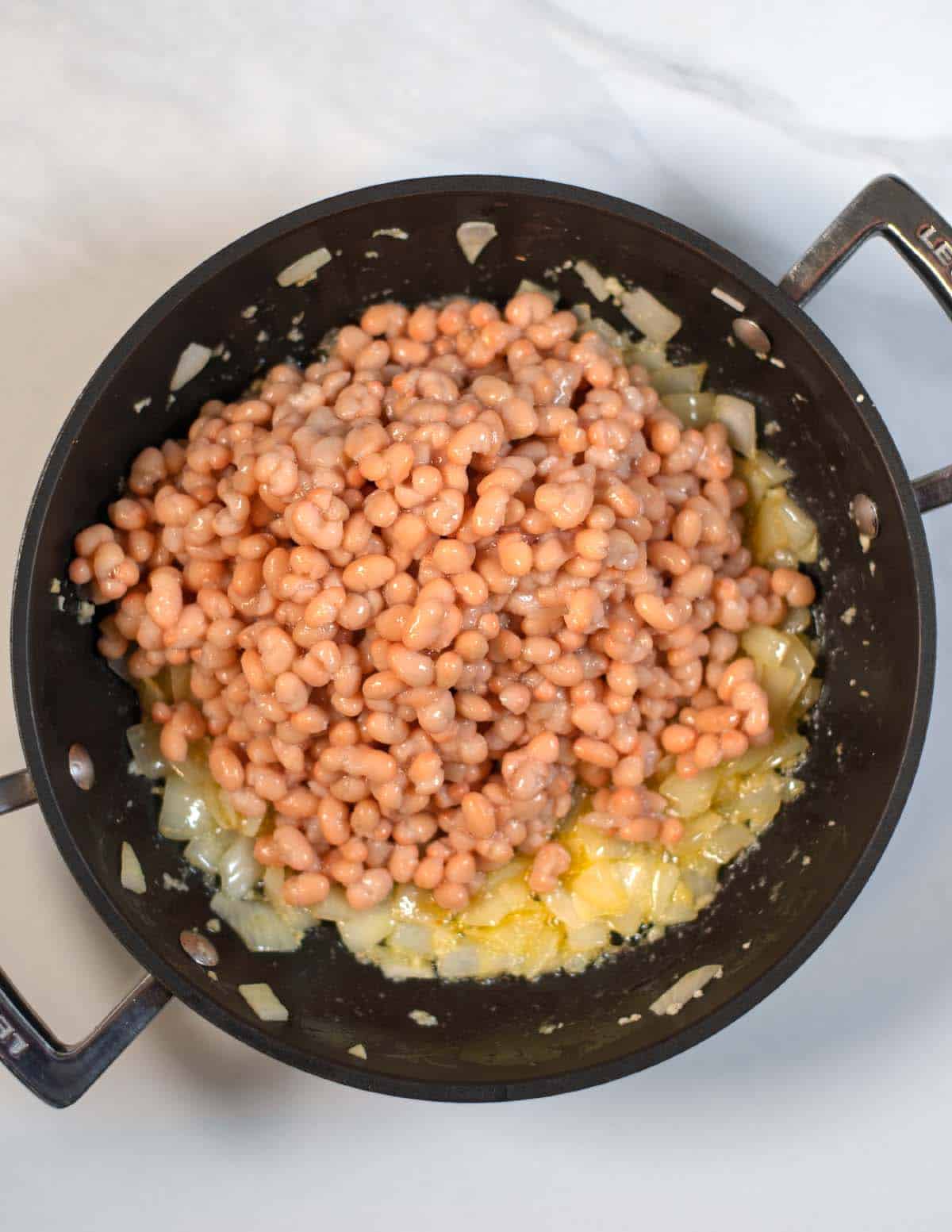 Canned white beans are given to a pan with onions.