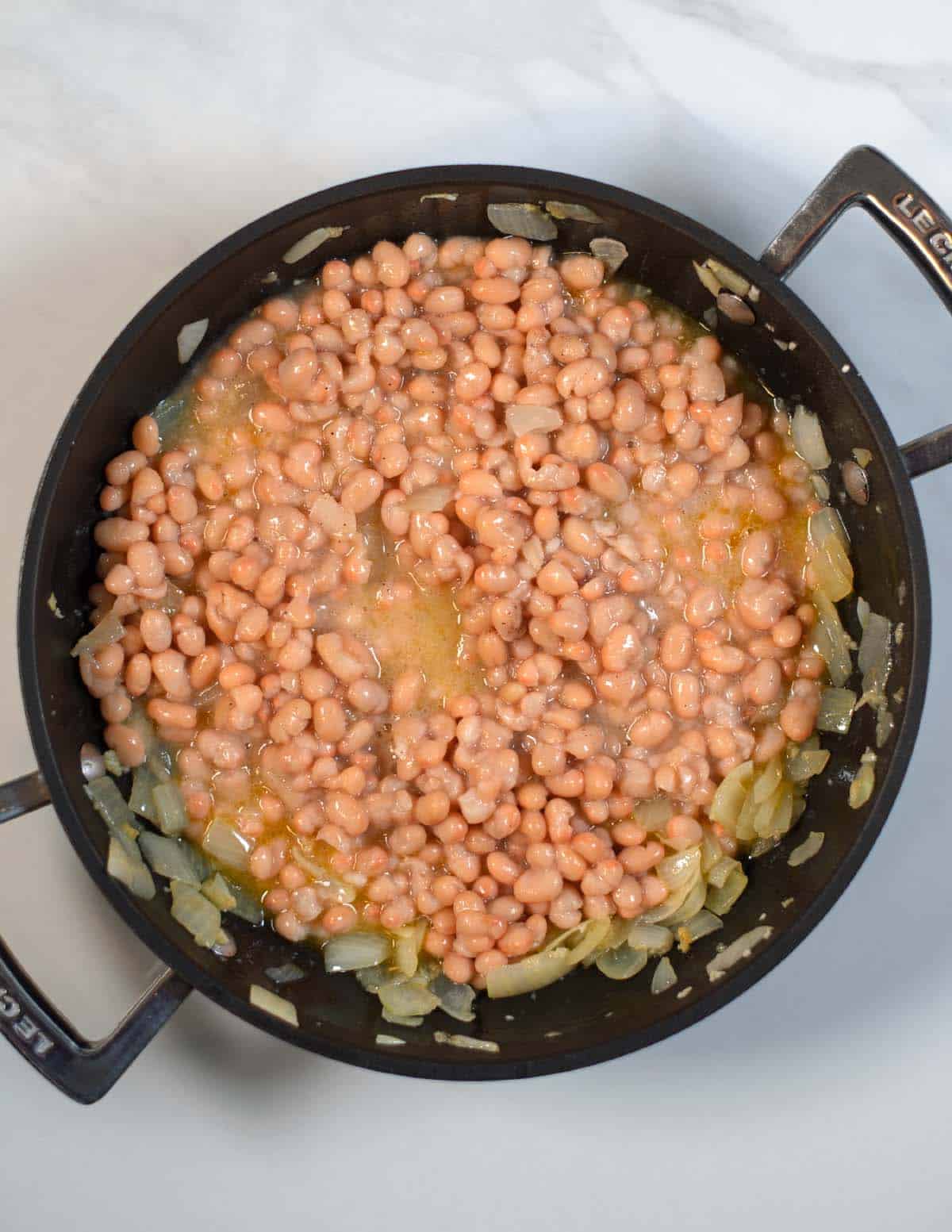 White beans have been mixed with onions in a pan.
