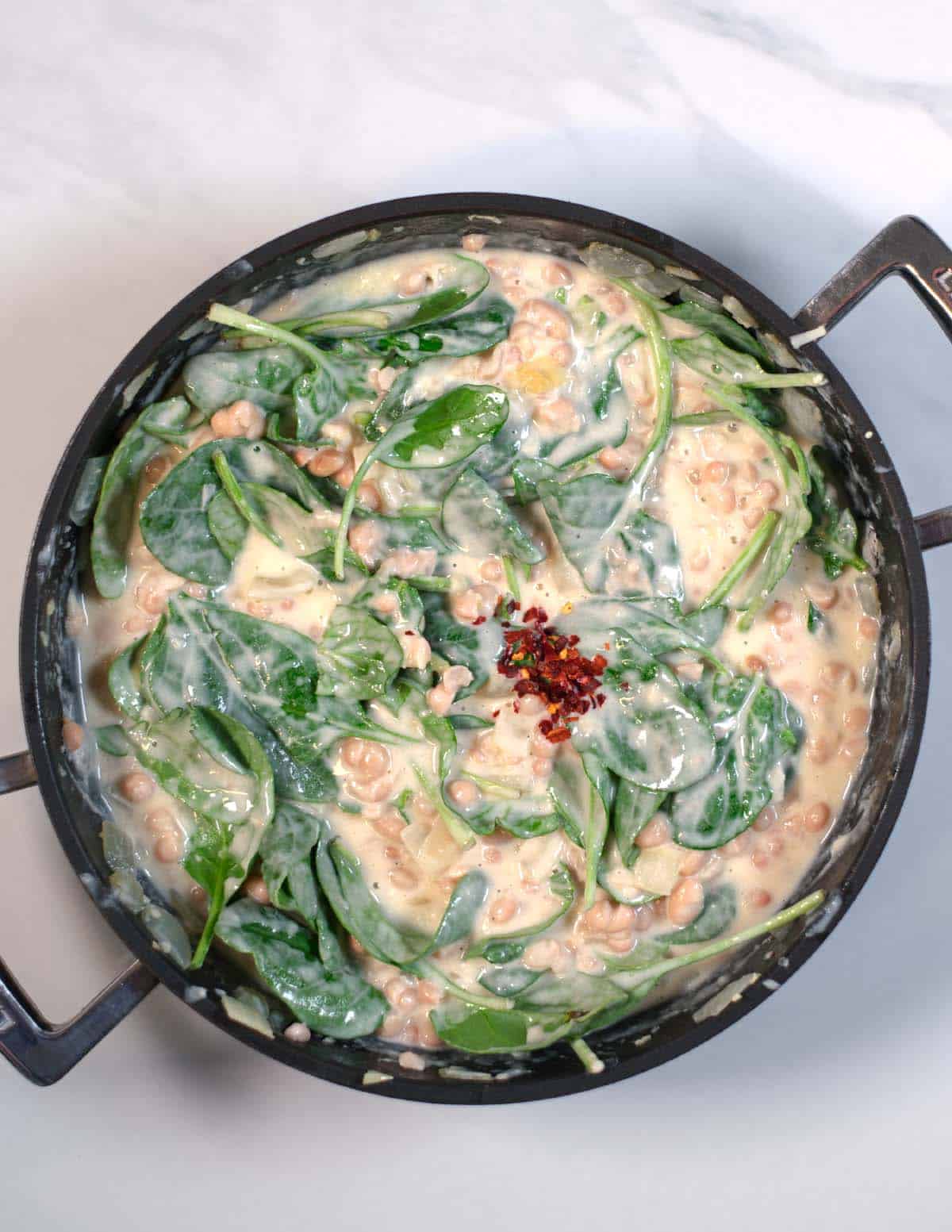 Fresh spinach leaves and red pepper flakes are added to the pan with creamy white beans.