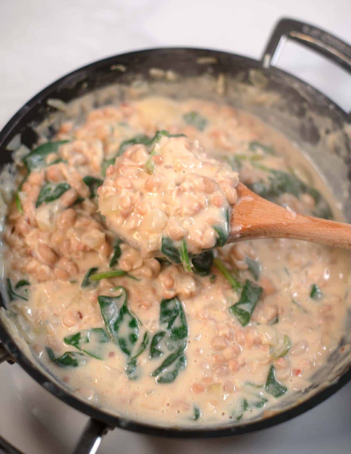 A wooden spoon lifts some of the Beans and Greens from the pan.