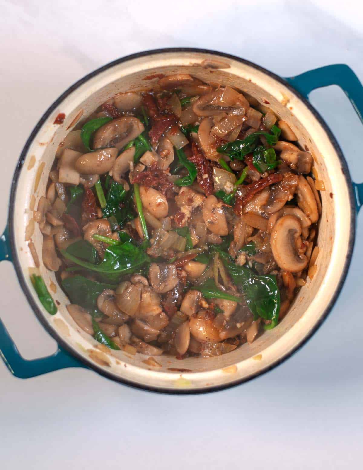 Wilted spinach, onions and mushrooms in the Dutch oven.