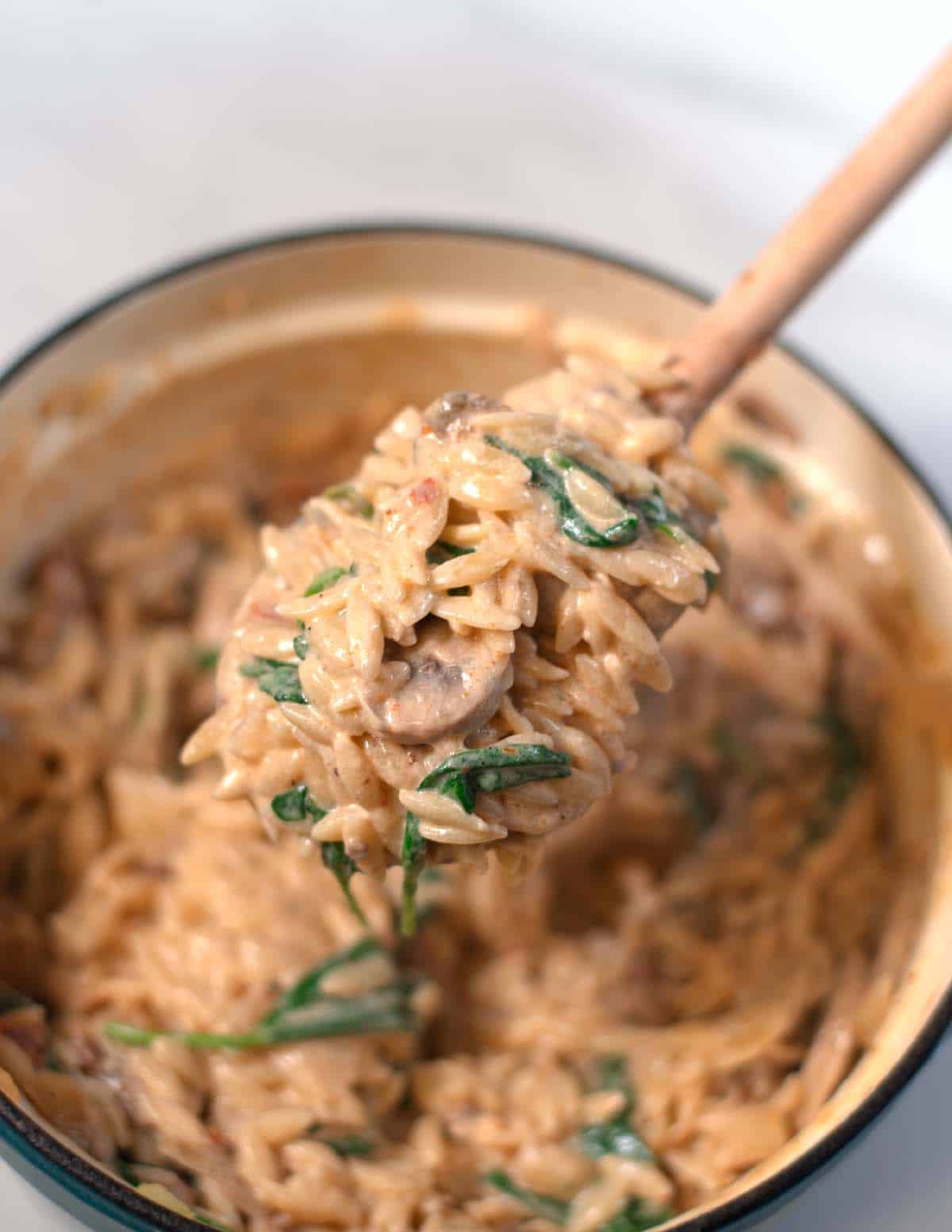 A wooden spoon lifts Marry Me Orzo from the Dutch oven.