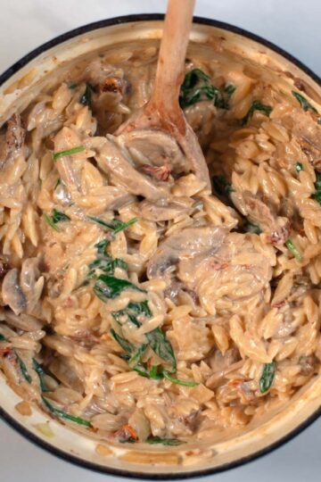 Preview picture of the ready Marry Me Orzo with spinach, a cremy sauce, and a wooden spoon.
