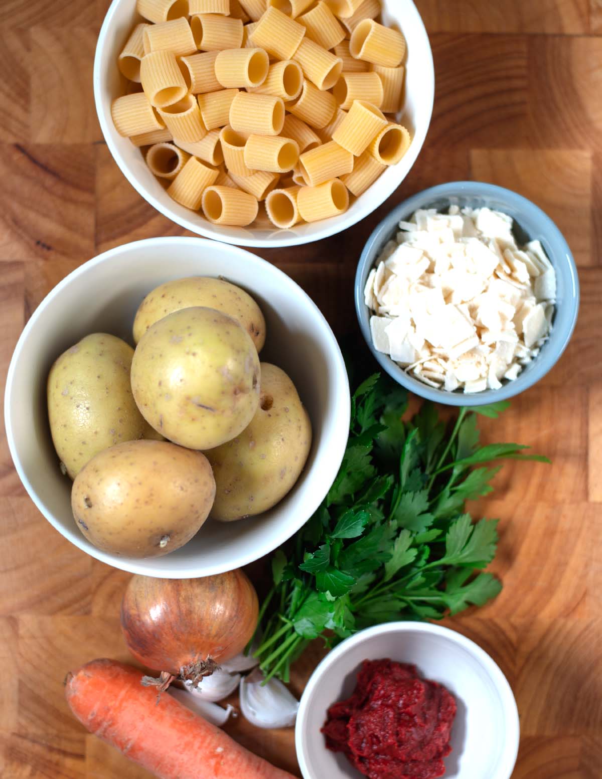 Ingredients needed to make Pasta e Patate are collected on a wooden cutting board.
