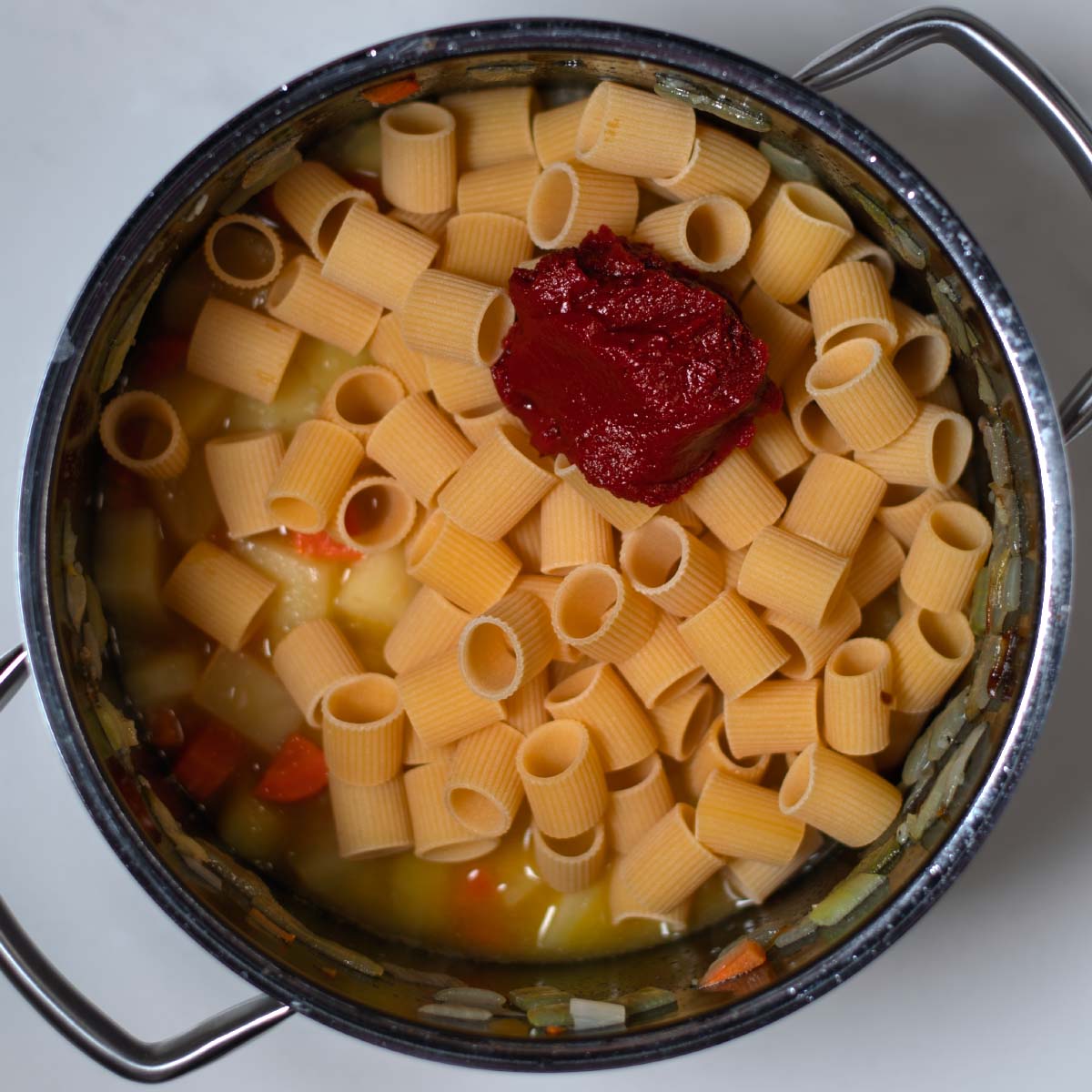 Tomato paste and liquids are mixed with the pasta and potatoes.