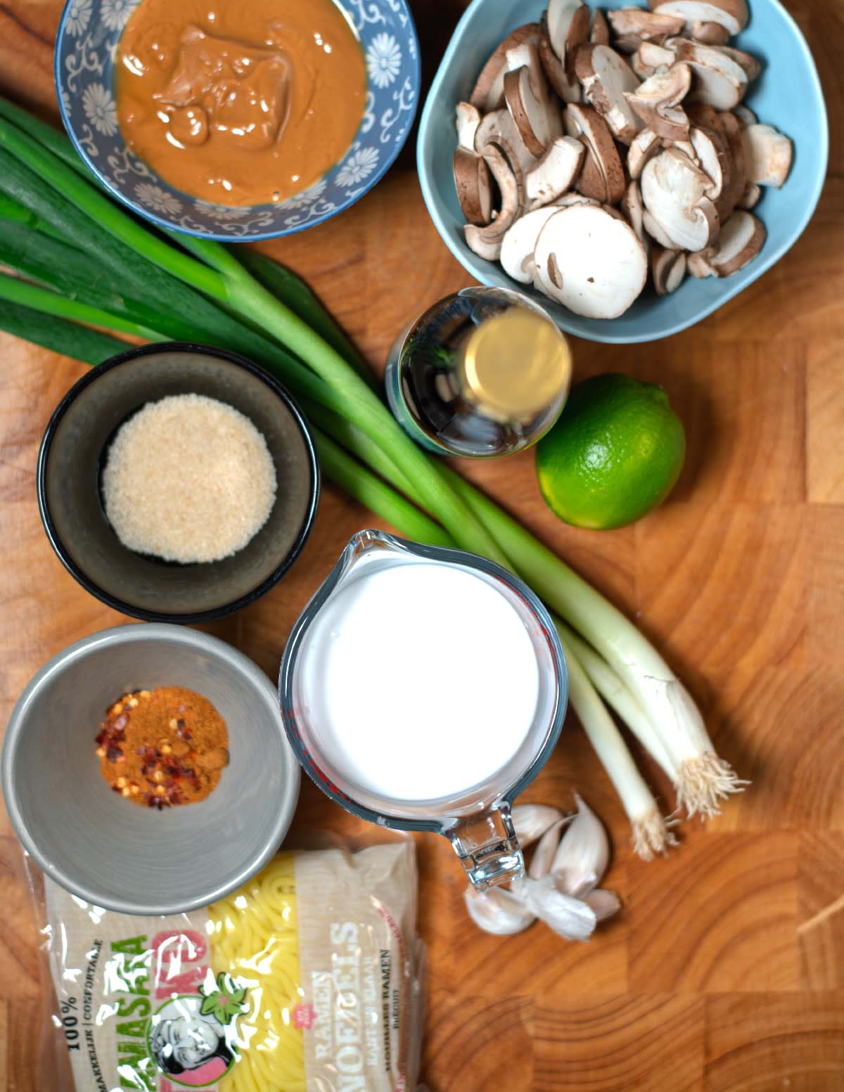 Ingredients needed to make Penaut Butter Ramen are collected on a wooden cutting board.