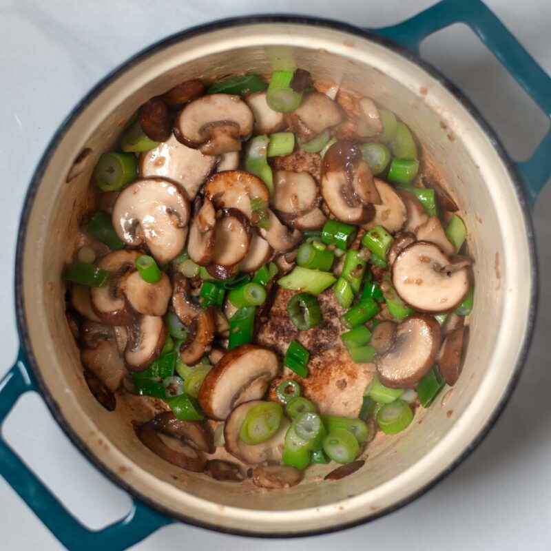 Mushrooms and green onions are fried in a Dutch oven.
