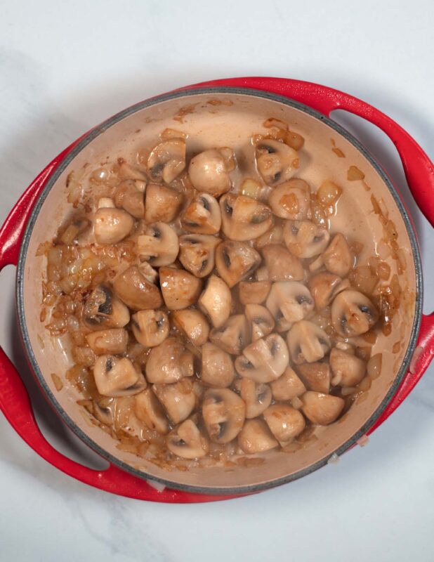 Quartered mushrooms are fried in a large pan.