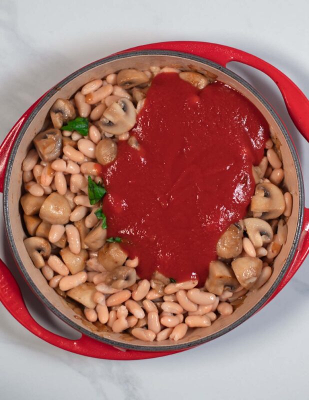 Tomato sauce and seasoning are added to the pan with the beans and mushrooms.