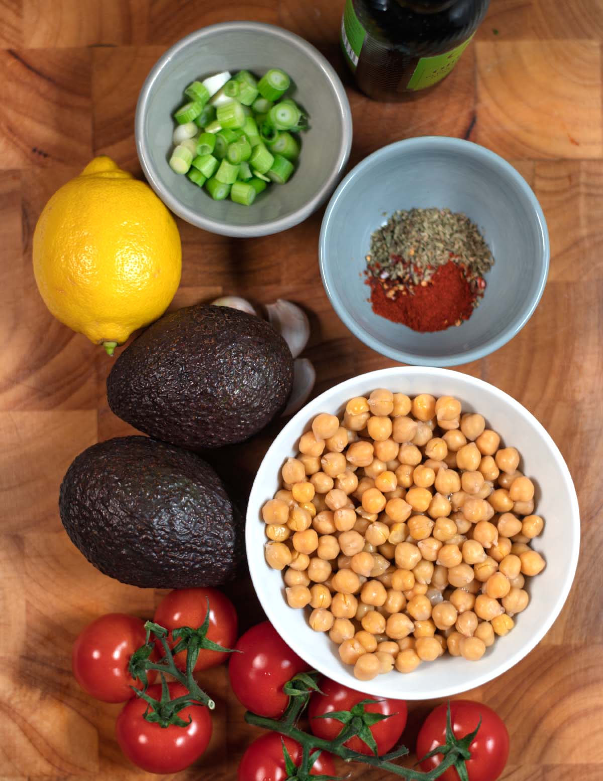 Ingredients needed to make Avocado and Chickpea Salad collected on a wooden board.