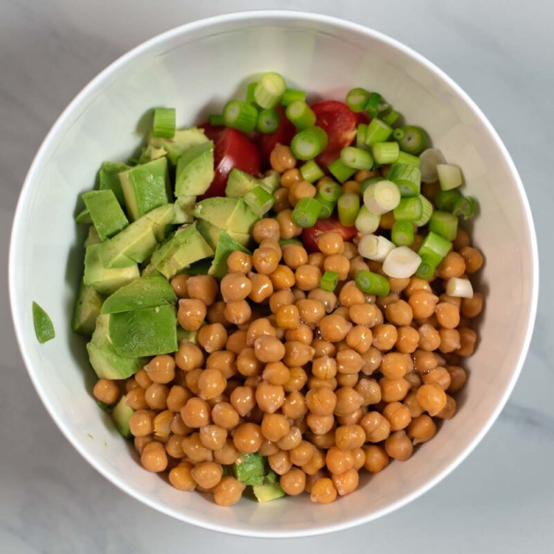 Scallions are added to the bowl with salad ingredients.
