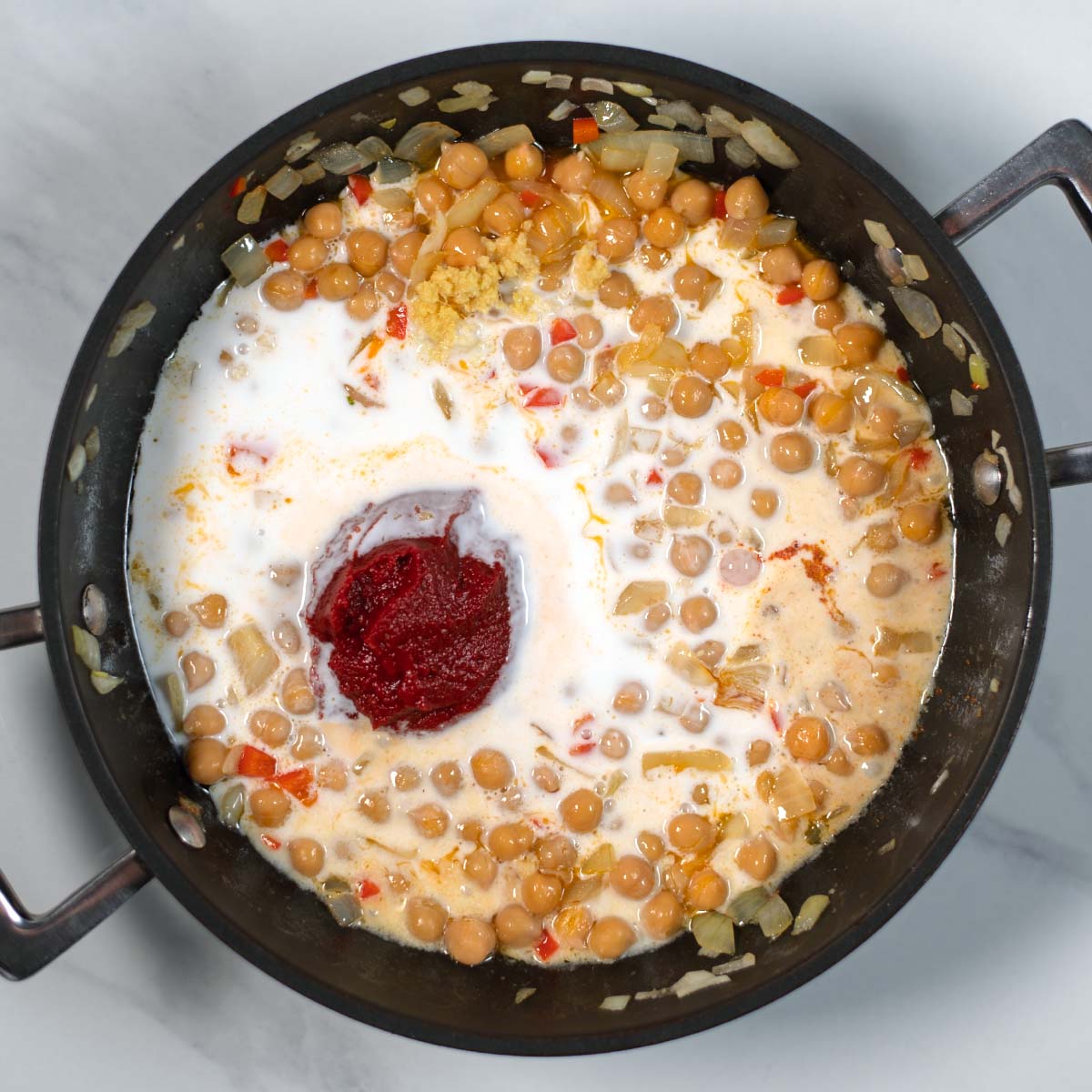 Tomato paste, spices, and coconut milk are given to the onion-chili mixture and chickpeas.