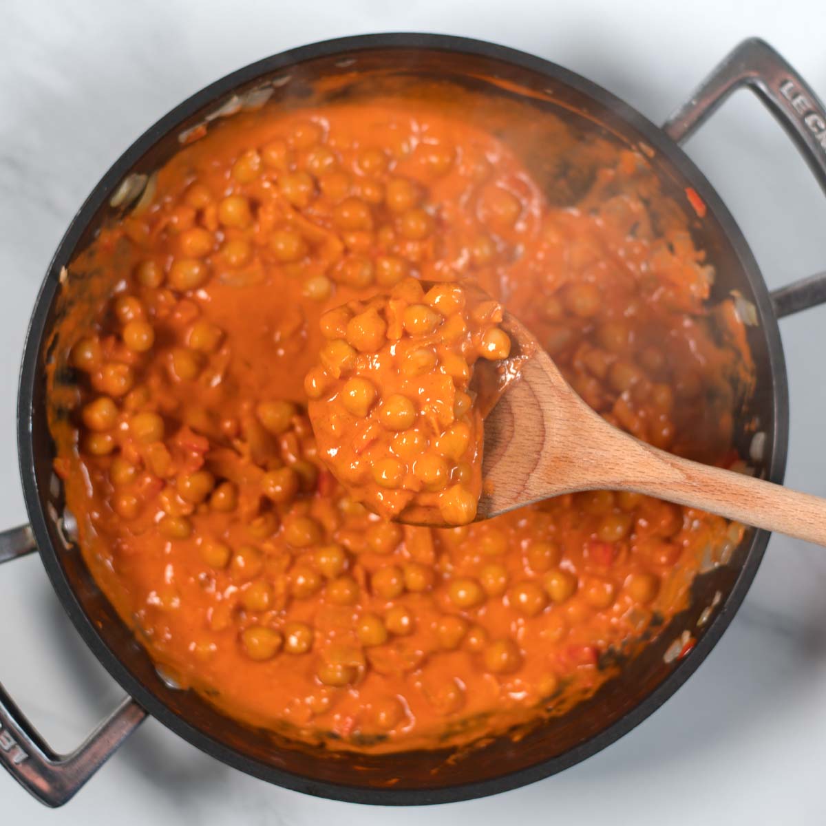 Wooden spoon lifts Butter Chickpeas from the pan.