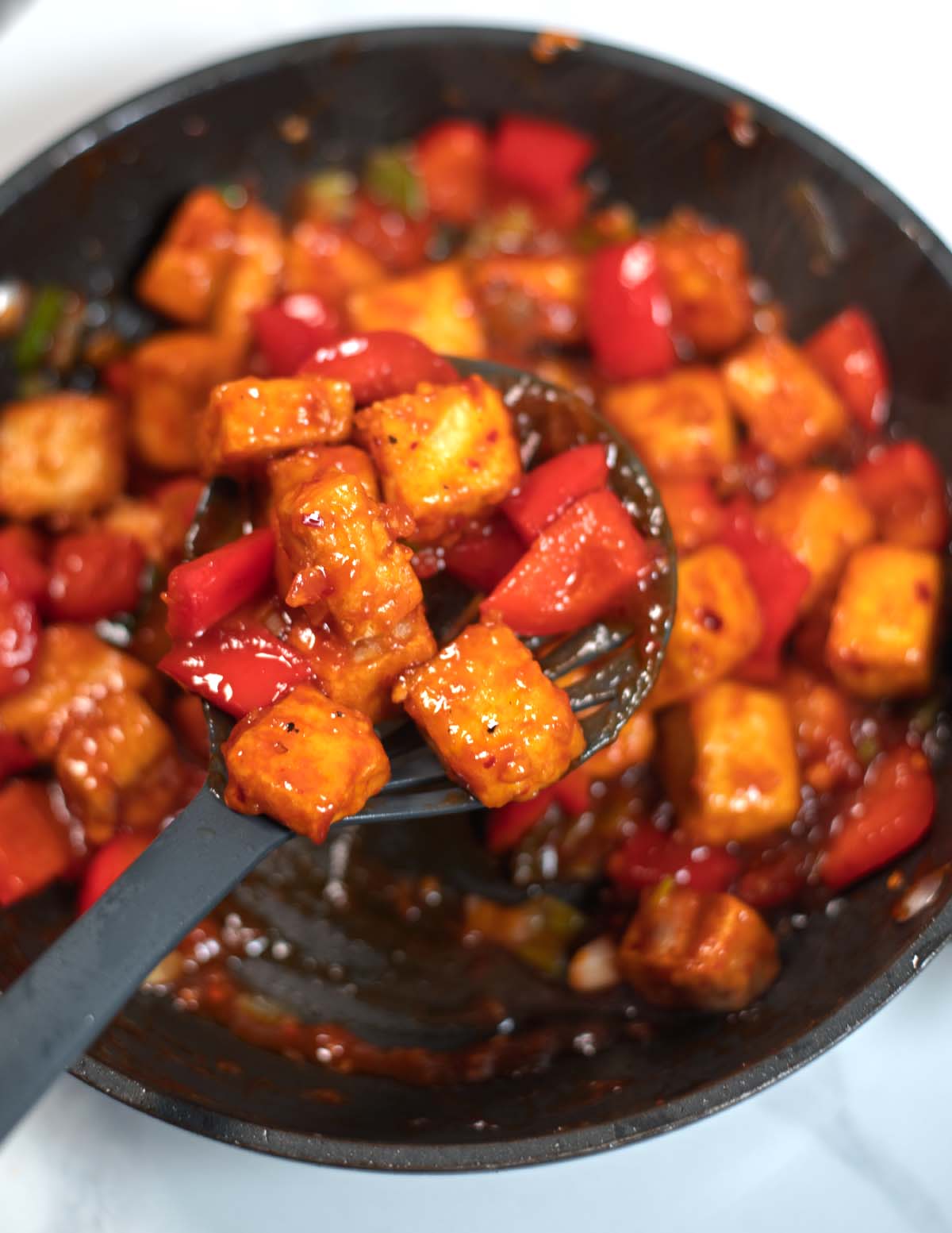 A large spoon lifts Chili Tofu from the pan.