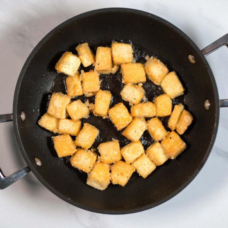 Tofu cubes are fried golden in a pan.