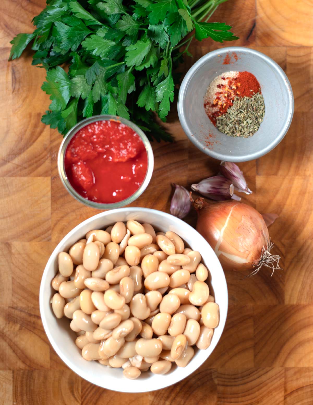 Ingredients needed to make Gigantes Plaki are collected on a wooden board.