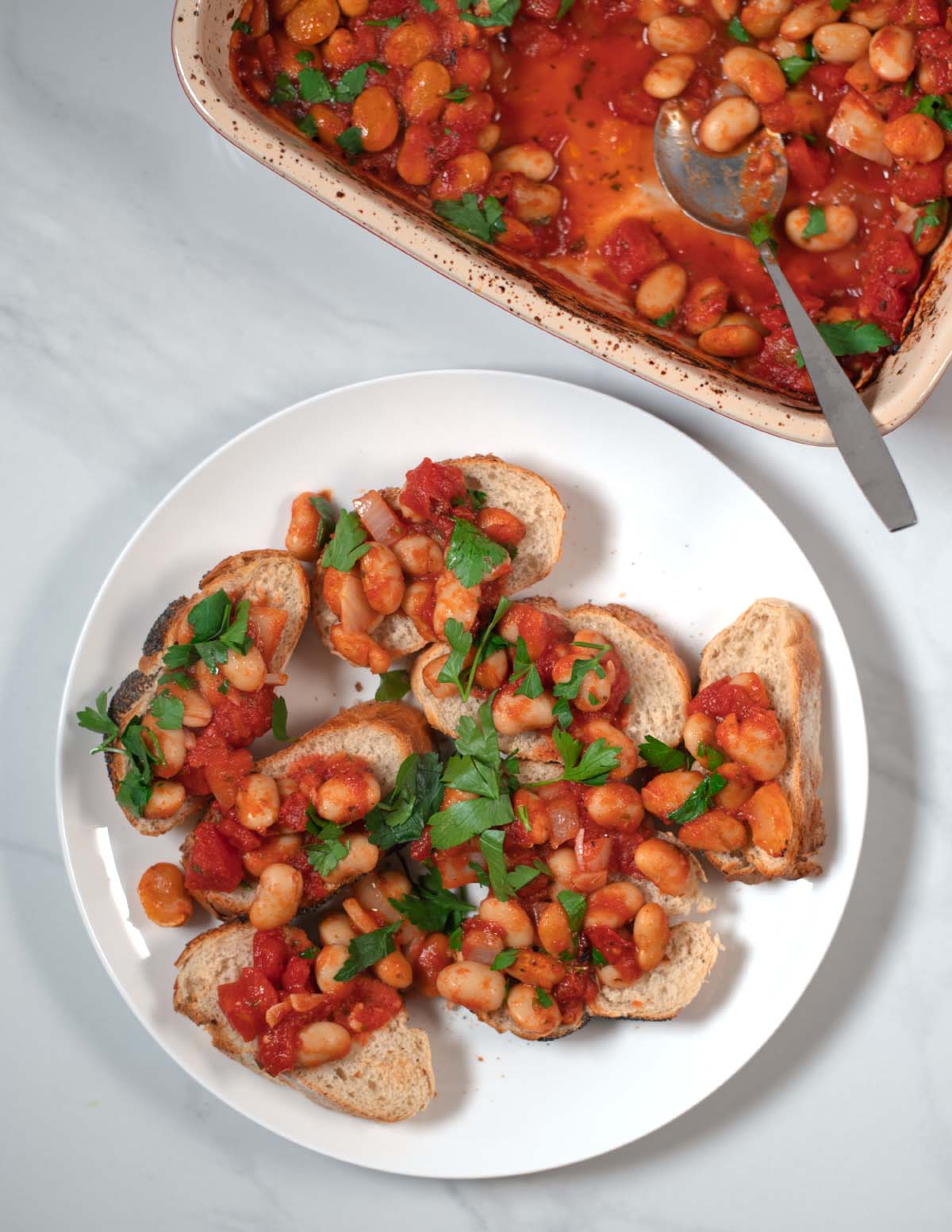 Servings of Gigantes Plaki with fresh bread on a white plate.