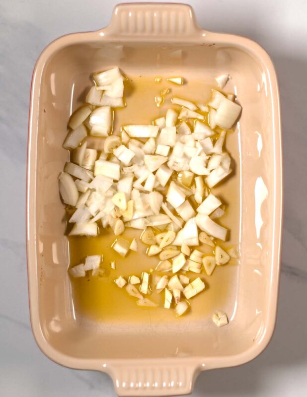 Chopped onions and garlic are given into a baking dish with oil.
