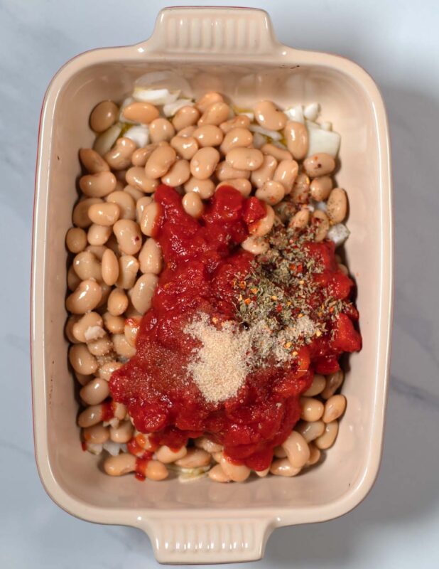 A spice mixture is given over diced tomatoes in a baking dish.