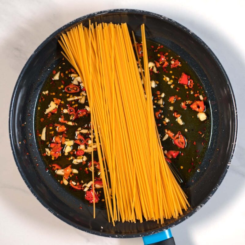 Uncooked spaghetti are given into the pan with smoky spices.