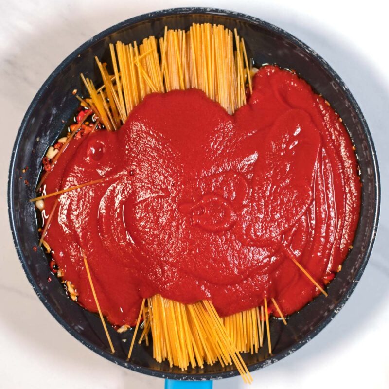 Tomato paste is given over the spaghetti in the pan with the spices.