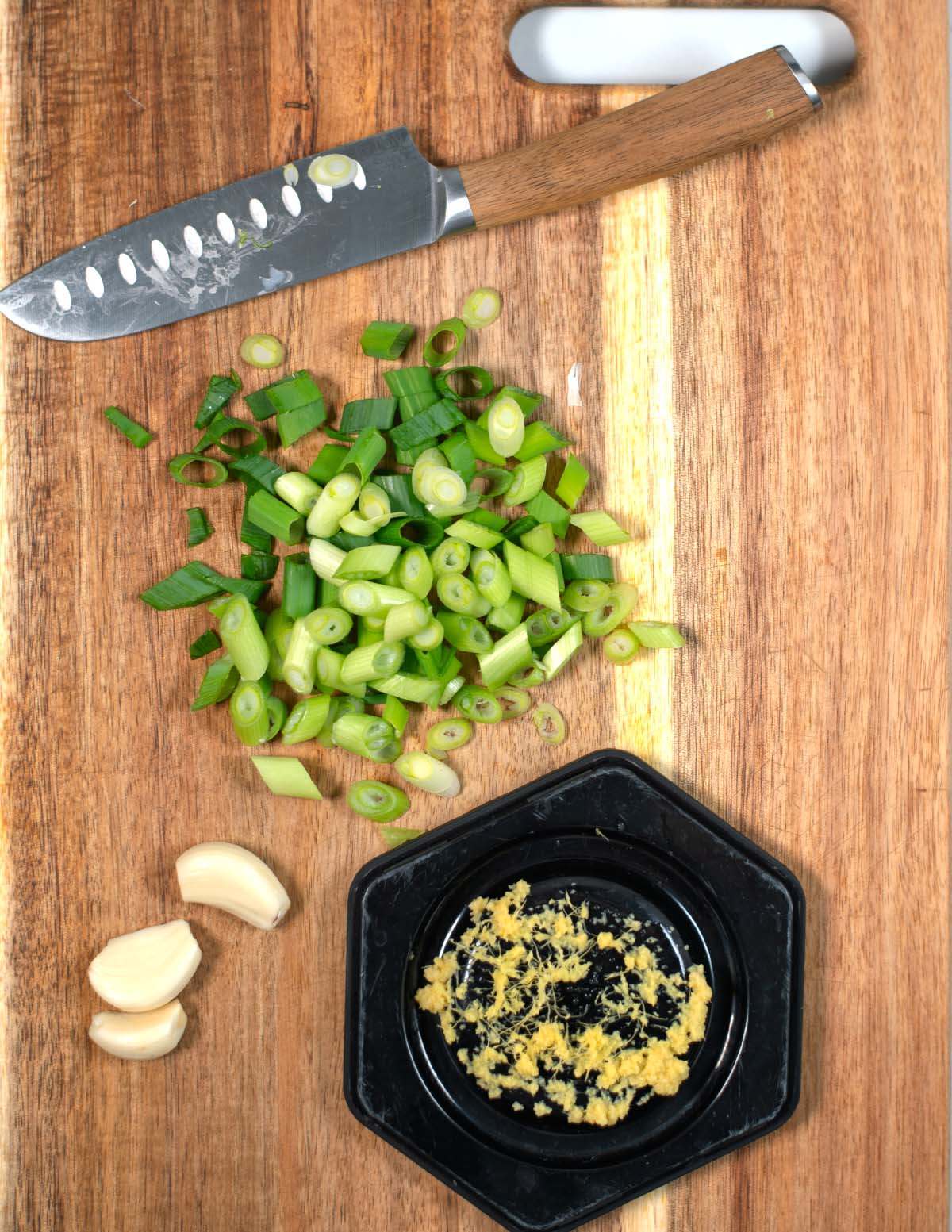 Cutting board and knife with chopped scallions, garlic, and ginger.