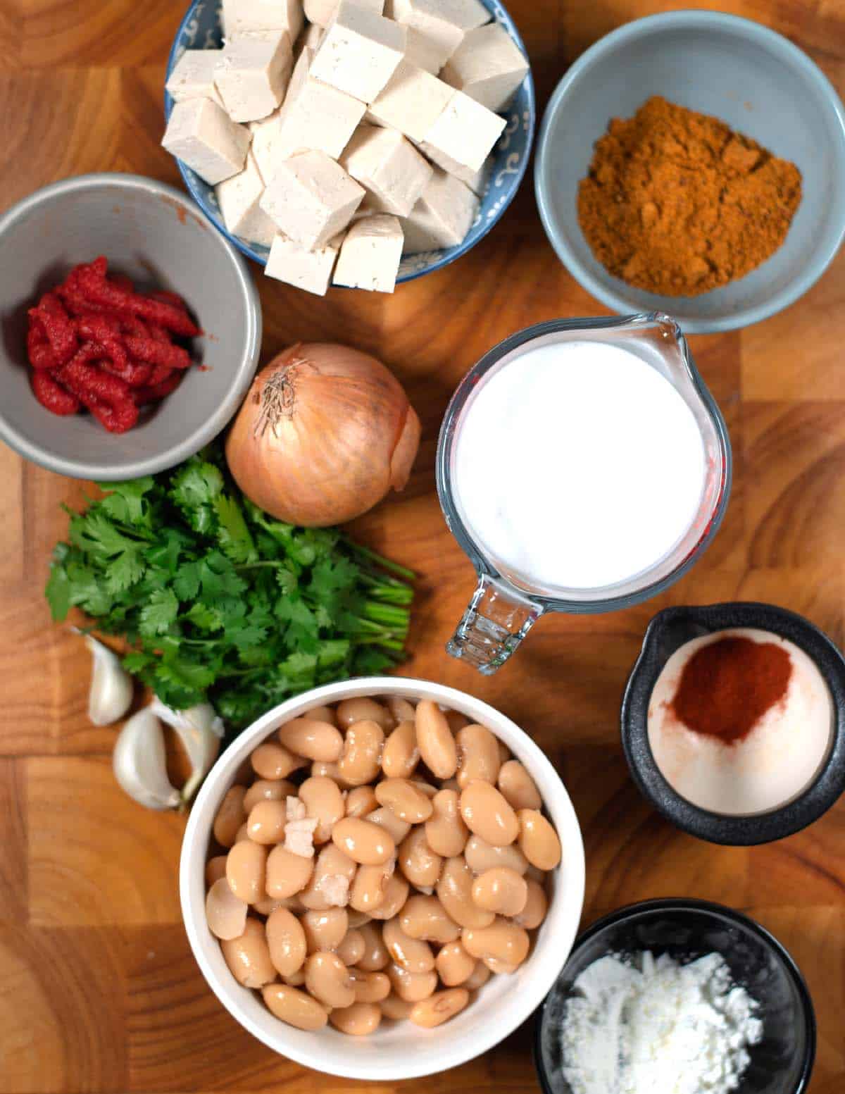 Ingredients needed to make Creamy Tikka Masala Beans are collected before preparation on a wooden board.