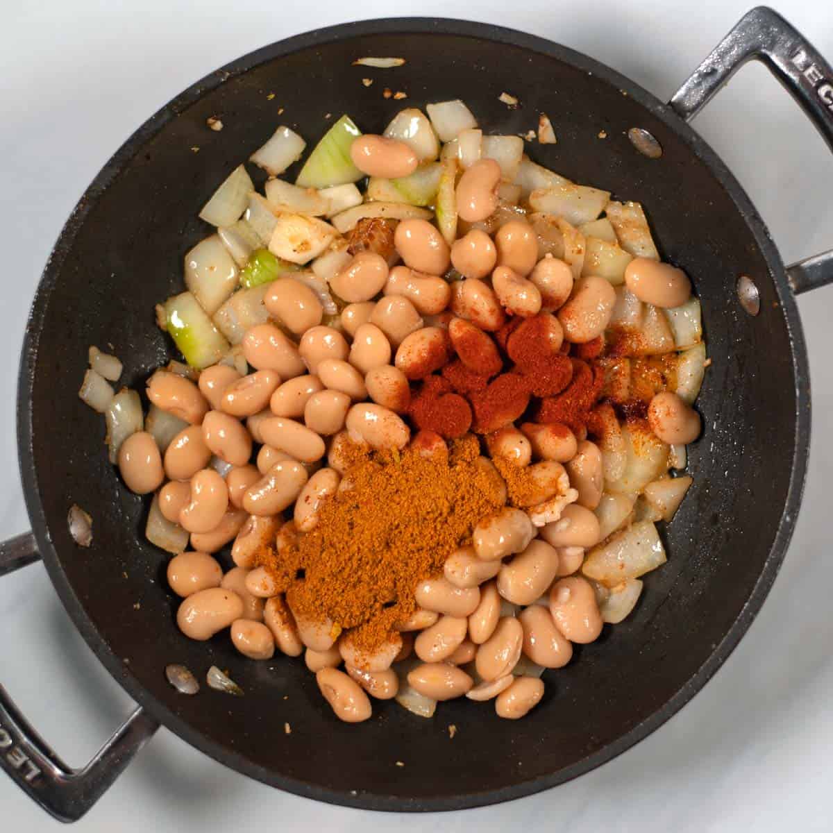 Beans, onions, spices are cooked in a pan.