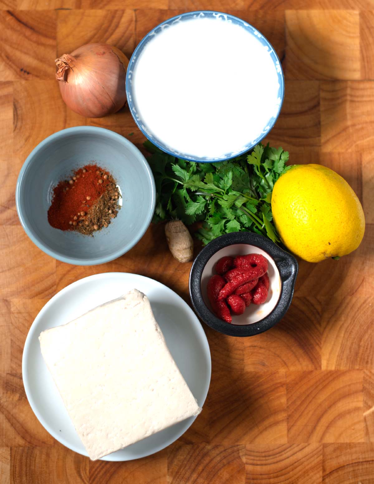 Ingredients needed to make Tofu Tikka Masala are collected on a wooden baord.