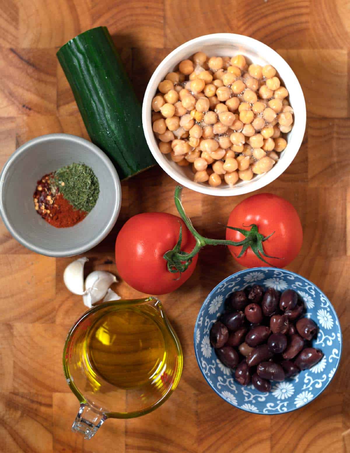 Ingredients needed to make Greek Chickpea Salad collected on a wooden board.