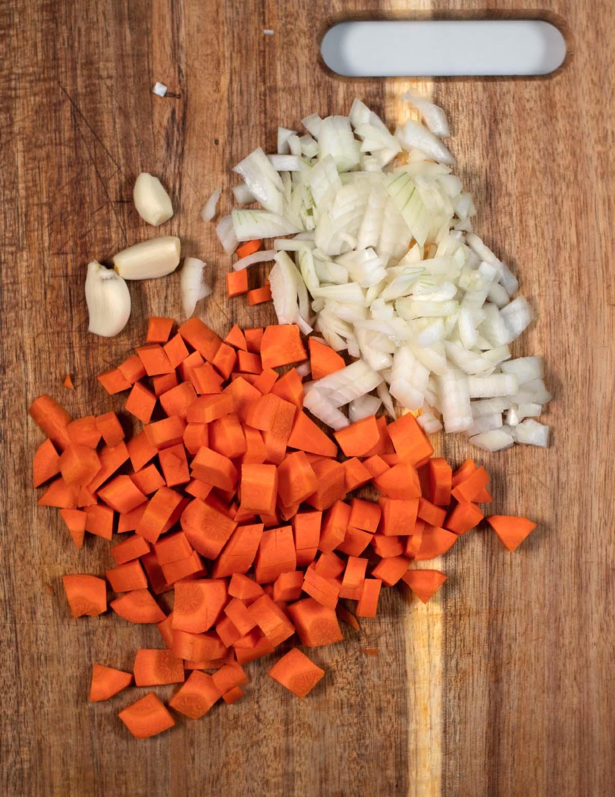 A cutting board with chopped onions and carrots, plus peeled garlic.