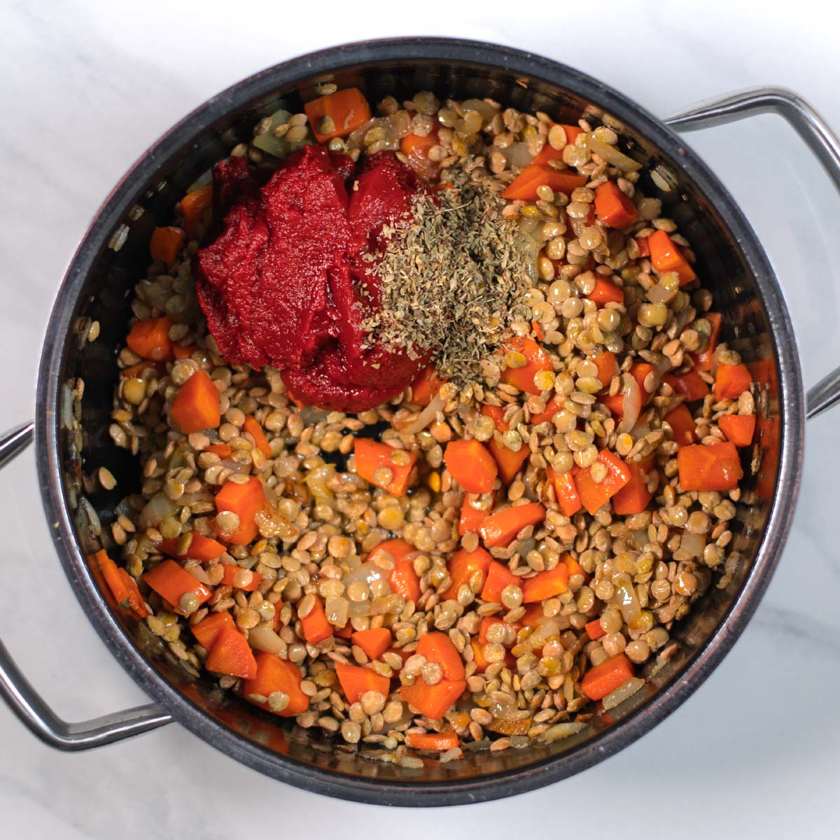 Lentils, tomato paste, spices are added to the pot with onions and carrots.
