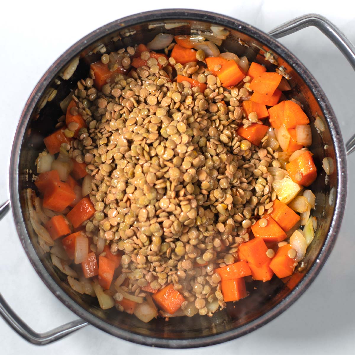 Onion, carrots, garlic, and lentils are cooked in a pot.