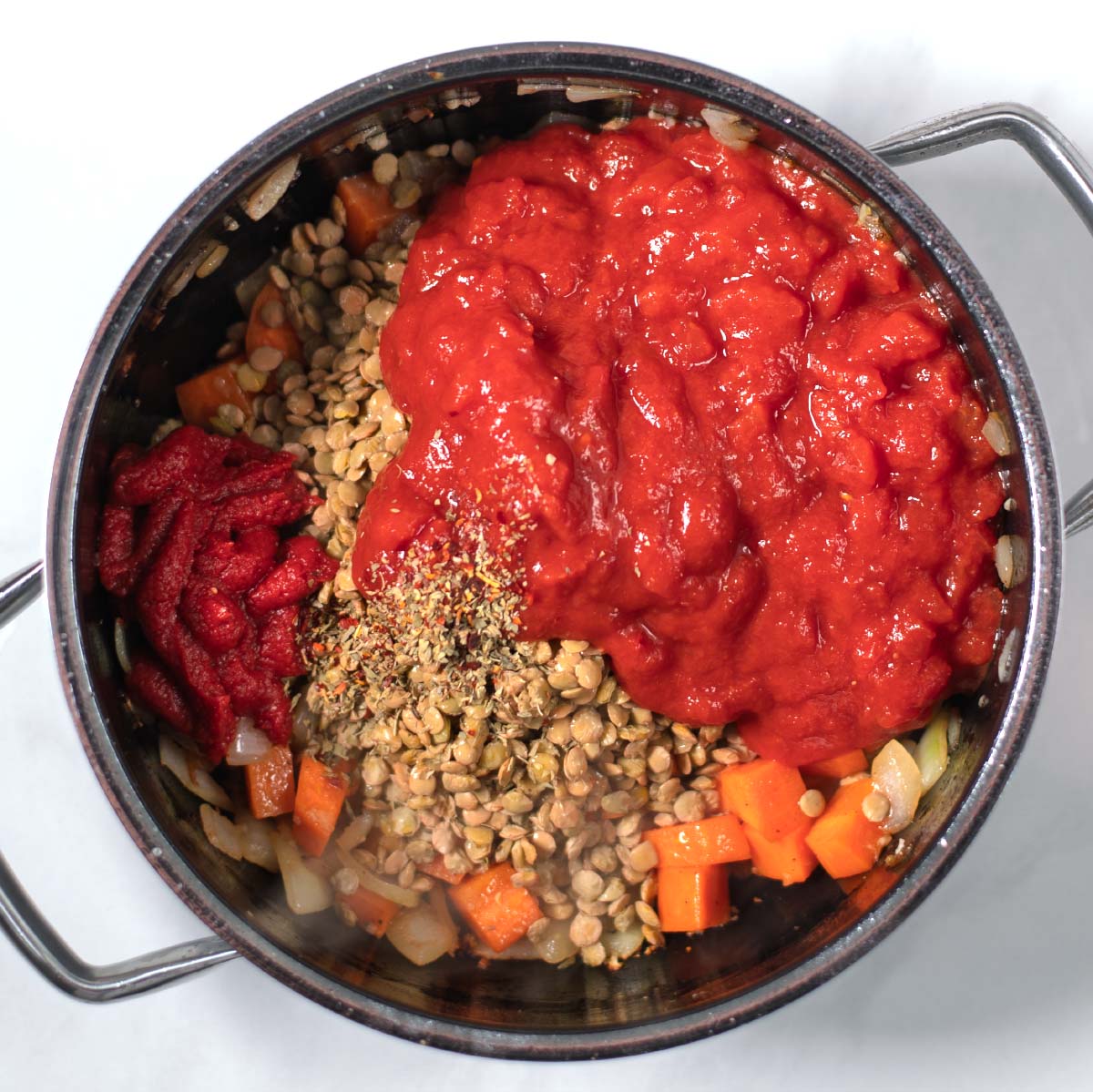 Tomato paste, diced tomatoes, and seasonings are given into the pot with lentils.