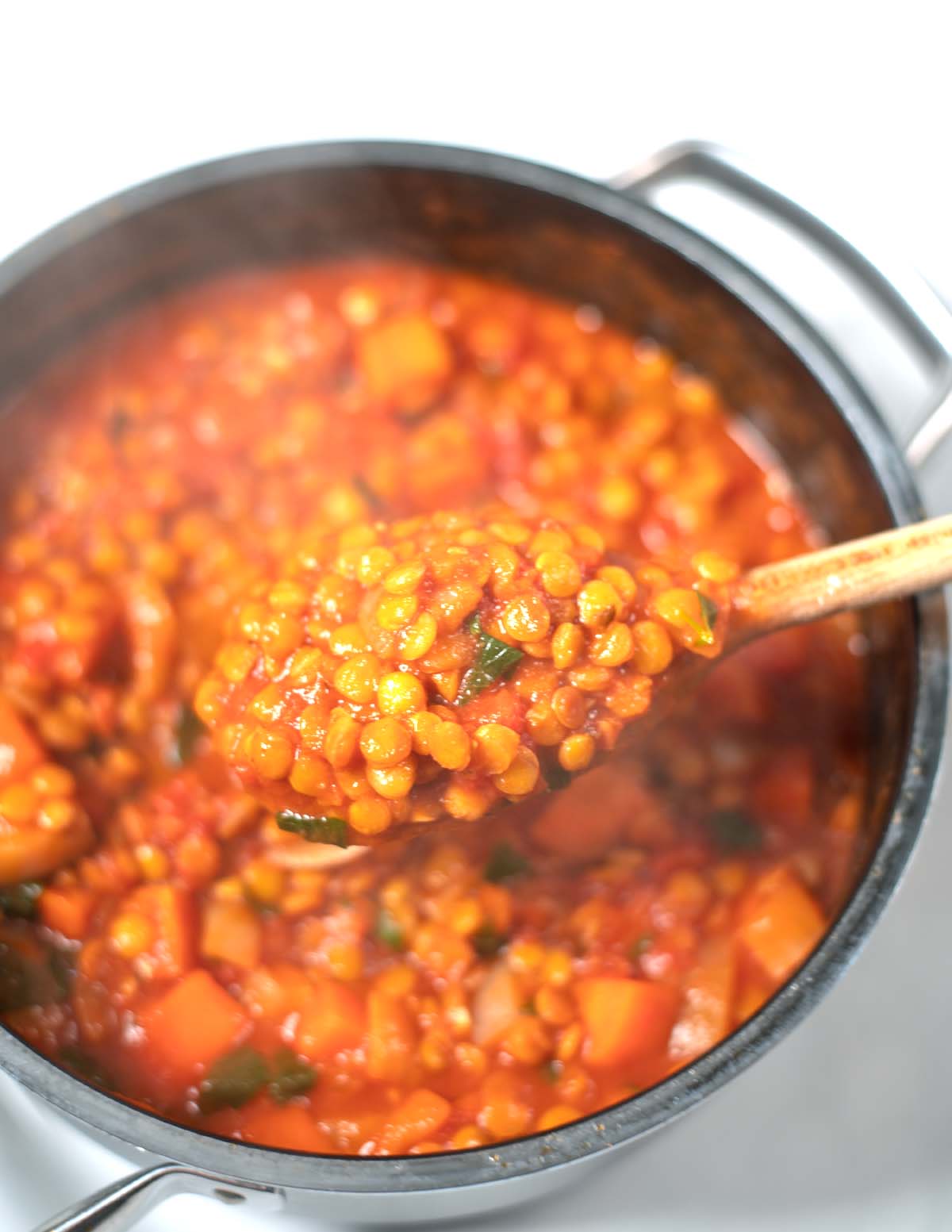 A large wooden spoon lifts Italian Lenil Soup from the big pot.