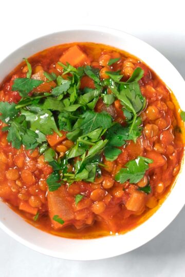 A serving of Italian Lentil Soup in a small white serving bowl, garnished with fresh parsley.
