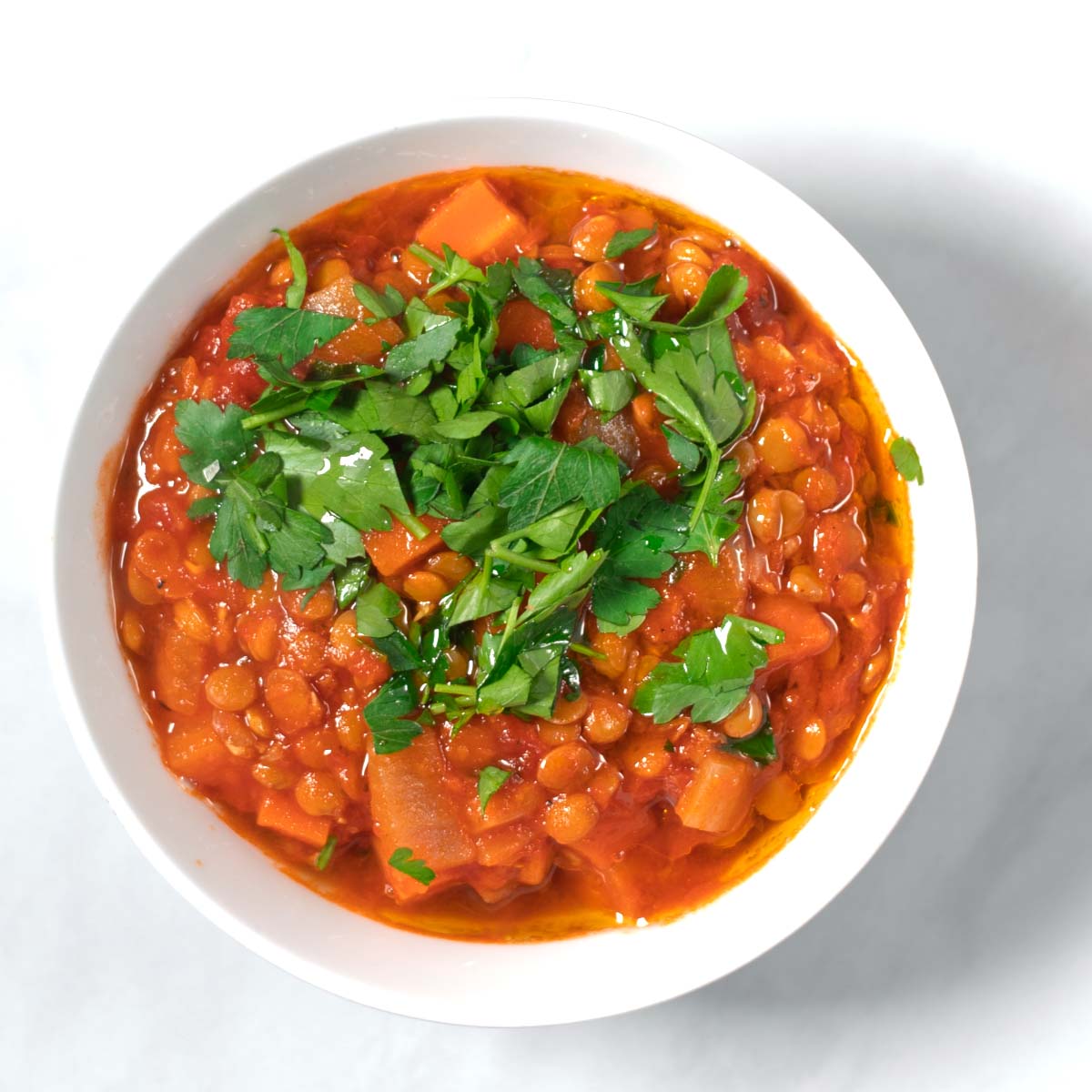 A serving of Italian Lentil Soup in a small white serving bowl, garnished with fresh parsley.