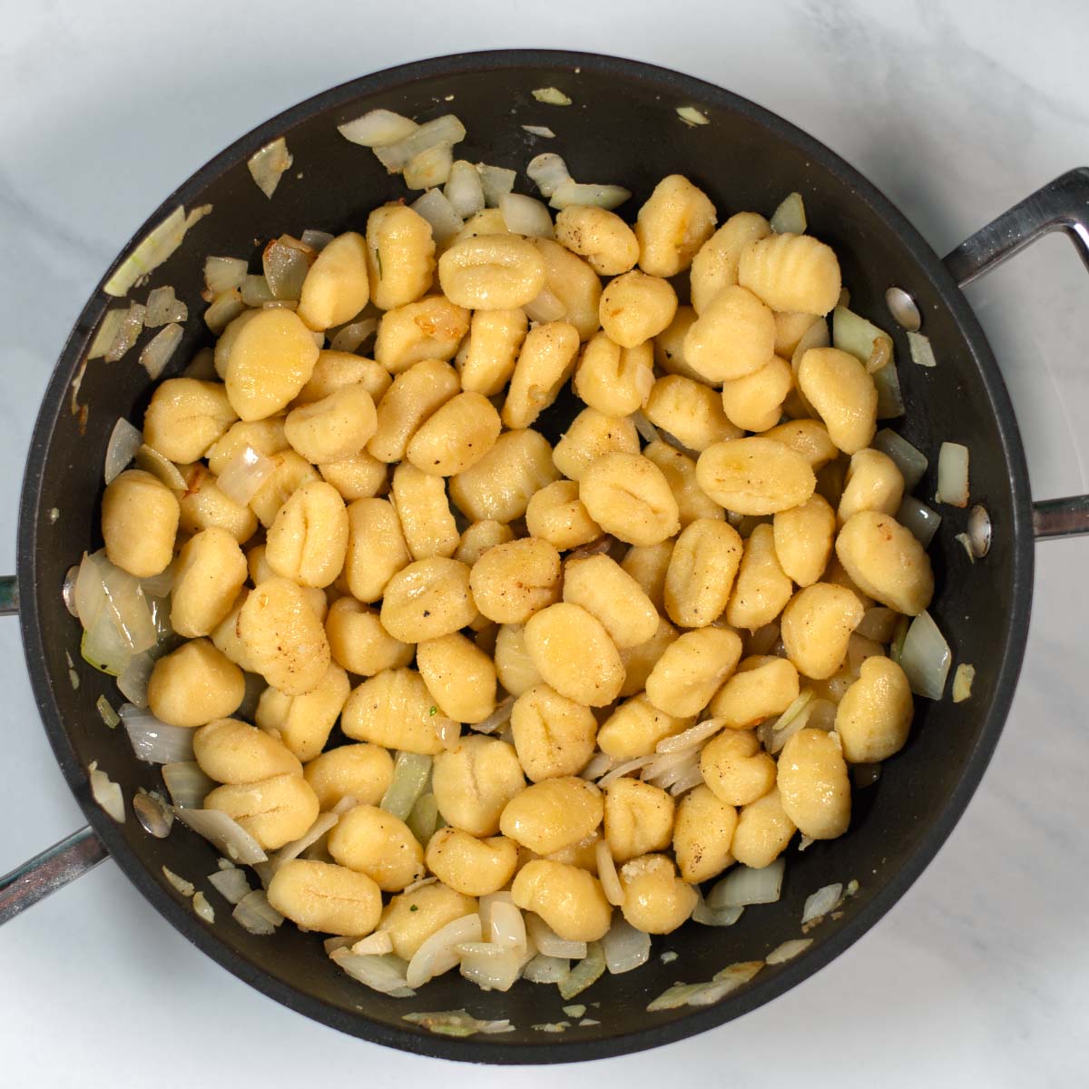 Onions and gnocchi are fried in a pan.