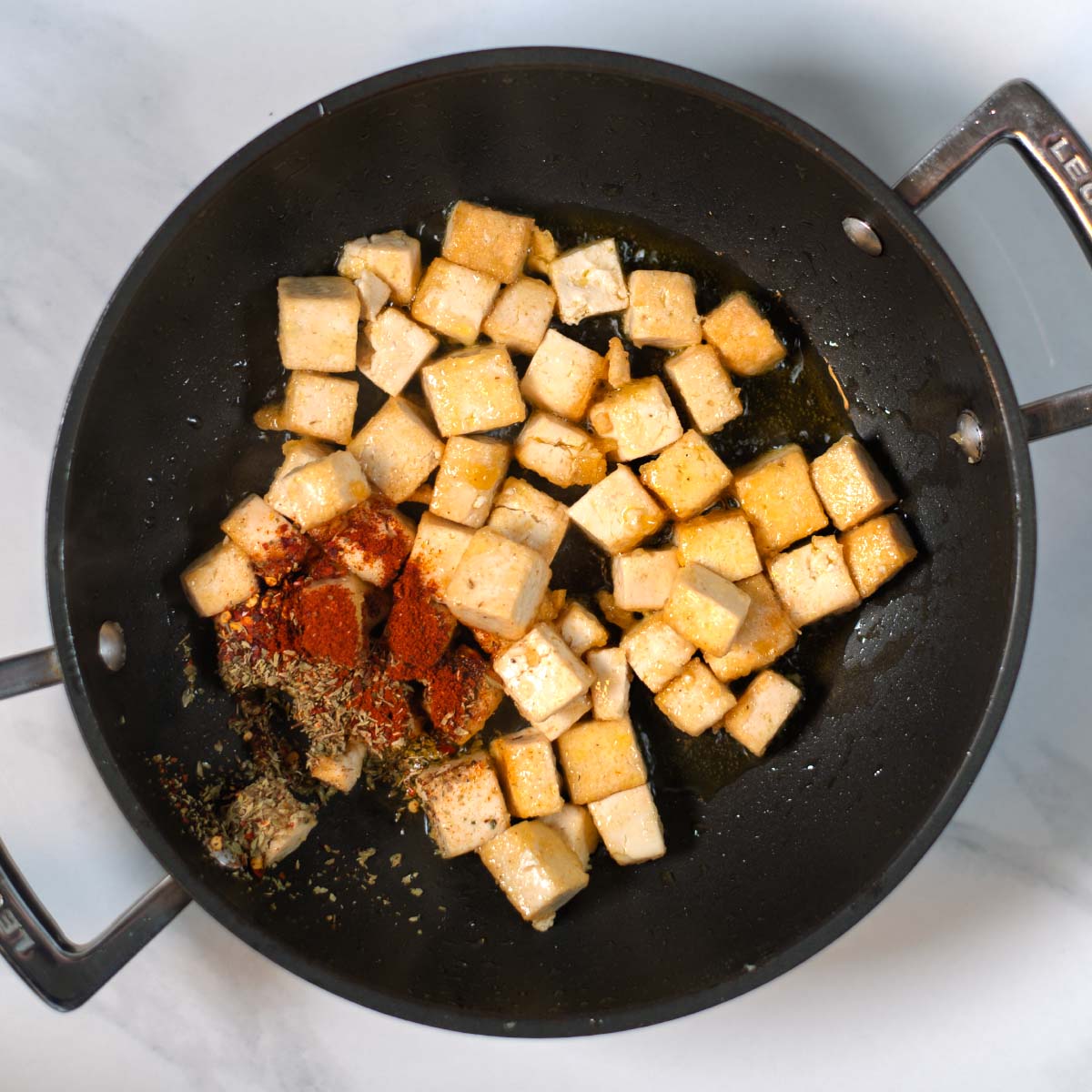 Cornstrach covered tofu cubes are fried in a pan and seasoned with spices.