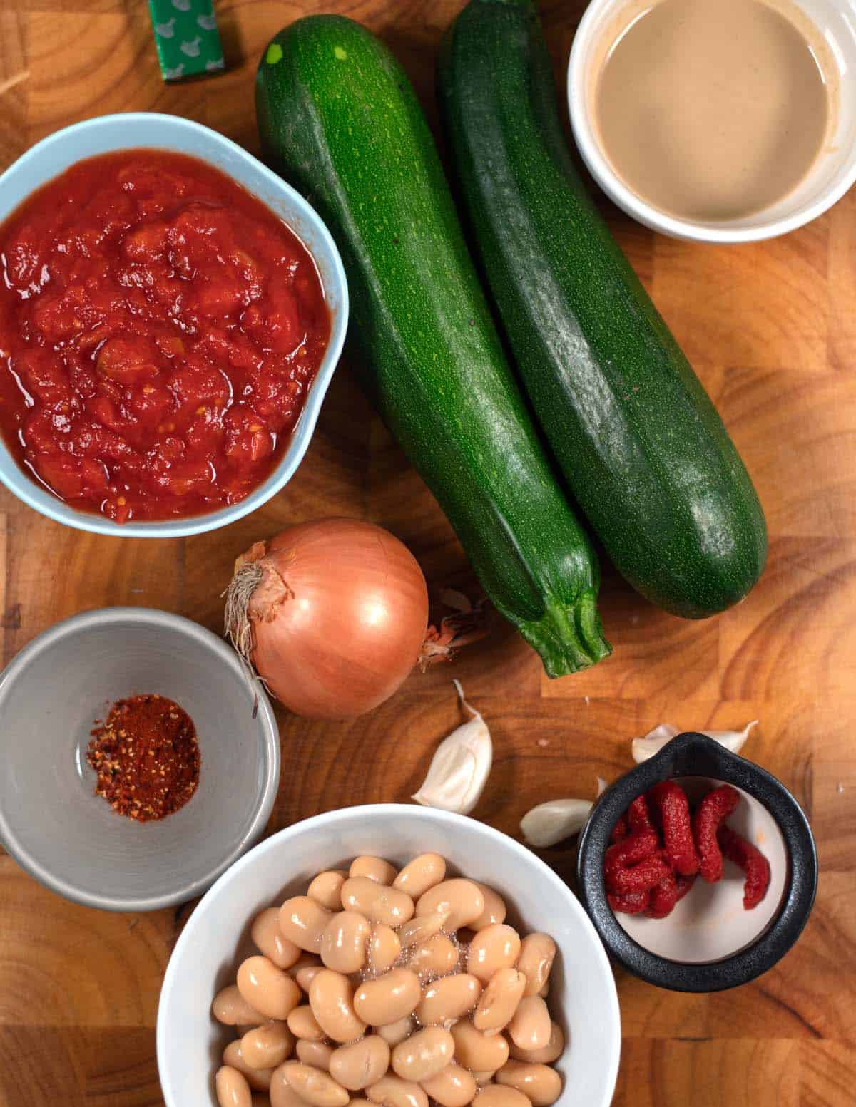 Ingredients that are needed to make Creamy Zucchini Stew with Tahini are collected on a wooden board.