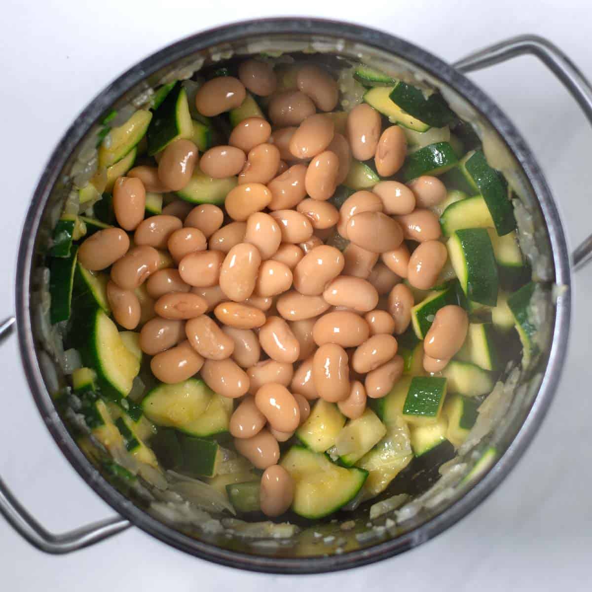 Onions and zucchini are cooked in a large pot, then butter beans are added.