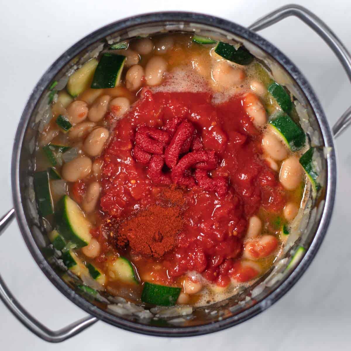 Diced tomatoes, tomato paste, and vegetable broth are given to the pot.